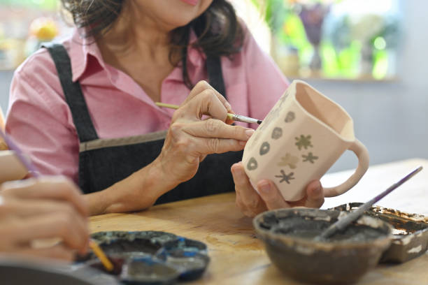 Close up and cropped image of An elderly potter painting and decorating the pottery.